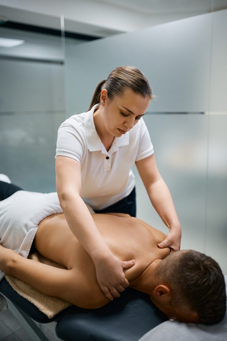 Swedish Relaxation Massage Camrose 3 Female massage therapist giving Deep Tissue Massage Camrose to a man's shoulder at physical therapy center at Camrose